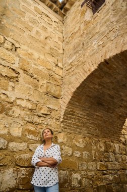 Puantiyeli bir kadın, taşralı bir duvara karşı düşünceli bir şekilde durup tarihi mimariye hayran kalır..