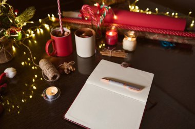 Tatil yaratıcılığı için sıcak, şenlikli bir sahne, kırtasiye malzemeleri, dekorasyonlar, mumlar ve kupalar ahşap bir masada. Noel temalı projeler ve mevsimsel ilham için mükemmel.