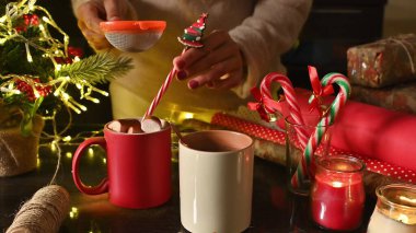 Warm holiday drinks are prepared amidst Christmas decor, with mugs, candy canes, and glowing candles enhancing the festive mood in a cozy ambiance. clipart