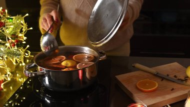 A cozy kitchen setting with mulled wine preparation using spices and fruits, complemented by warm holiday lighting and decor. clipart