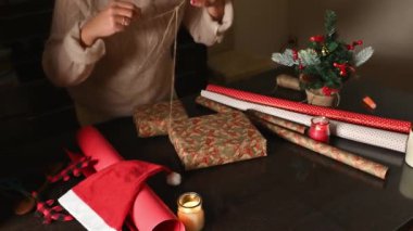 Noel hediyelerini kırmızı kâğıt ve iple saran bir kişi..