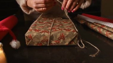 Tatil tasarımlarıyla süslü bir kağıda sarılmış bir hediyeye sicim bağlayan eller. Tatil sezonu hazırlığı.