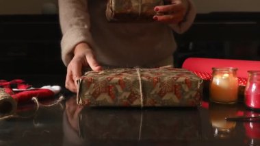 Kutlama malzemeleriyle, mumlarla ve dekoratif eşyalarla bir masaya hediyeler saran bir insan, rahat bir tatil ortamı yaratıyor..