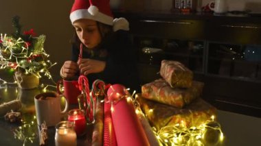 Noel Baba şapkası takan bir çocuk Noel hediyeleri ve süslemelerle süslenmiş bir masada oturur..