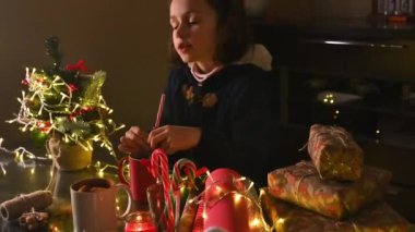 Küçük bir çocuk Noel hazırlıklarını hediyeler, şekerler ve sıcak ışıklarla yapıyor. Sahneyi sarılı hediyeler, dekore edilmiş bir minyatür ağaç ve bayram hediyelerinin yer aldığı şenlikli bir ortam kaplıyor..