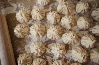 Un kaplı bir yüzeye dikkatlice yerleştirilmiş el yapımı khinkali hamur tatlısı. Geleneksel Gürcistan hamur köfteleri, bölgenin ev yapımı mutfağının pişirilmeye hazır olduğunu gösteriyor..