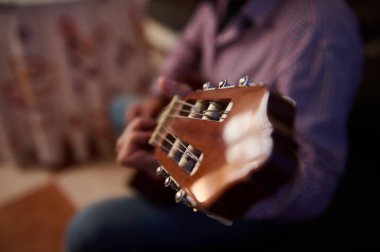 A close view highlighting the guitar head and tuning pegs as someone plays it in an indoor setting. The image conveys a sense of musical passion, concentration, and creativity. clipart