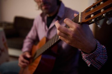 A closeup view of a person playing an acoustic guitar indoors, emphasizing relaxed and focused engagement during practice or performance. The scene creates a calm and inspirational ambiance for music lovers. clipart