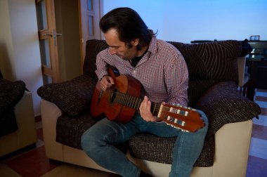 Bir adam evdeki rahat bir kanepede otururken akustik gitar çalar. Ayarlama bir rahatlama hissi verir ve kişisel alandaki müzikal ifade ve yaratıcılığa odaklanır..