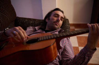 Sıcak ve rahat bir ortamda akustik gitar tıngırdatan bir adam. Sahne müzikal yaratıcılık, kendini ifade etme ve sakin bir iç gözlem anı öneriyor..