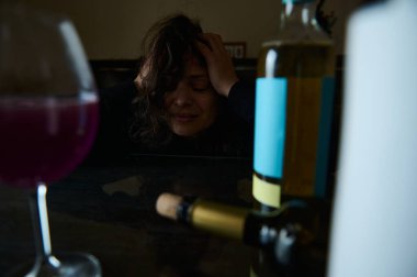 A distressed woman sits at a table with wine bottles and a glass, portraying emotional turmoil and struggles with alcohol-related issues in an intimate and expressive setting. clipart