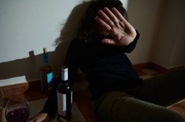 Loş bir odada yere oturmuş reddedildiğini göstermek için elini kaldıran bir insan. Çevrelerinde alkol şişeleri, alkol kullanımı ve farkındalık anlarıyla ilgili sorunları sembolize ediyor.