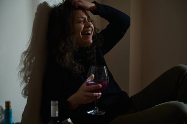 Neşeli bir kadın duvarın karşısında oturmuş, gülüyor ve elinde bir kadeh kırmızı şarap tutuyor. Bu görüntü rahatlamayı, mutluluğu ve gündelik bir andan zevk almakla ilgili kutlama duygularını temsil eder..