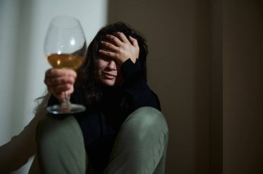 A seated individual holds a glass of wine with a somber and reflective expression. The scene conveys emotions related to introspection, loneliness, and sobriety, emphasizing the importance of alcohol awareness and wellbeing. clipart