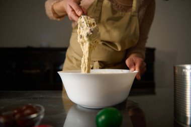 A person dressed in an apron kneads dough in a white bowl, evoking comfort and homeliness. clipart