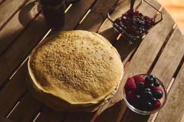 Taze böğürtlenler ve bir kase reçel eşliğinde ahşap masaya konmuş bir yığın taze hazırlanmış krep sıcak, sıcak, doğal bir kahvaltı ya da brunch anını sergiliyor..