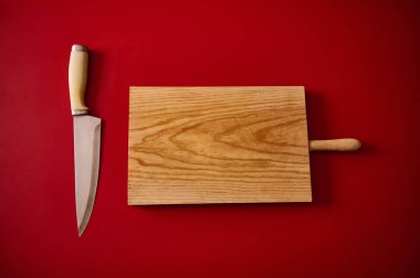 Temiz bir tahta kesme tahtası ve parlak kırmızı bir masa yüzeyine yerleştirilmiş keskin bir bıçak..