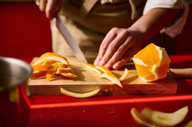 Bir insan, ahşap bir kesme tahtasına portakal kabuğunu dikkatlice keser ve mutfak hazırlıklarını yakalar..