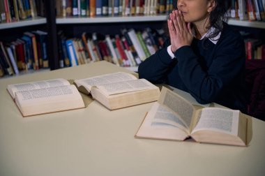 A focused individual sitting at a library desk with open books, symbolizing learning and research in a serene and knowledgeable environment. Reflects concepts like education, concentration, and clipart