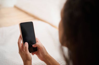 Kapalı alanda akıllı telefon kullanan bir kişinin yakın plan çekimi, cihazın ekranını odak noktasında vurgulamak, rahatlamış bir çevrede bir teknoloji kullanımı görüntülemek.