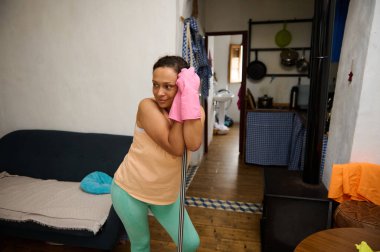 Eldiven giyen bir kadın, sıcak bir ev ortamında temizlik yaparken dinlenir..