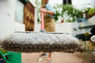 Arka planda yeşillik olan bir alanı temizlemek için kirli süpürge kullanılıyor.