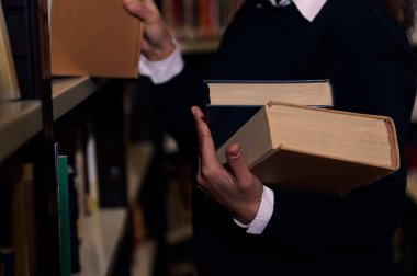 A person organizing, selecting books from library shelf, emphasizing learning and knowledge. The image captures the essence of research and accessibility of resources for academic or personal growth. clipart