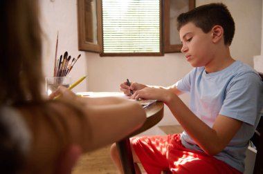 Genç bir çocuk ahşap bir masada otururken bir sanat eseri yaratmaya odaklanır..