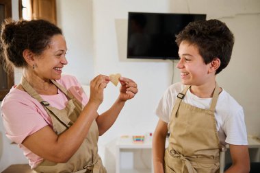 A joyful mother and her son share a fun moment baking in their aprons, fostering family bonds and creativity in a warm kitchen environment filled with love and laughter. clipart