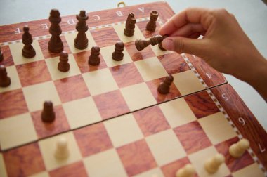 An individual's hand holding a chess piece on a wooden board during a game, symbolizing strategy and focus. clipart