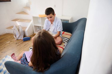İki çocuk, oyuncaklarla çevrili rahat bir oturma odasında oturuyor ve iletişim kuruyor..