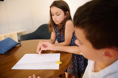 Two children collaborating on a worksheet together at a wooden table in a calm setting, focusing and sharing ideas. clipart