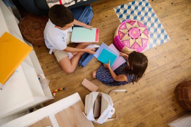 Renkli okul malzemelerini düzenleyen, eğitim hazırlığı, işbirliği ve takım çalışmasını destekleyen iki çocuk, rahat ve yaratıcı bir ev ortamında oturuyorlar..