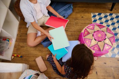 İki çocuk ahşap bir zeminde oturmuş ellerinde renkli defterler tutarak yaratıcılık ve işbirliği tasvir ediyorlar..