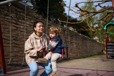 Bir anne ve küçük oğlu güneşli bir günde salıncakta sallanırken parkta birbirlerine bağlanıyorlar..
