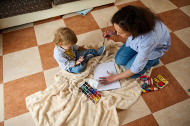 A mother and her child enjoy arts and crafts on a comfortable blanket, surrounded by toys and creative materials, fostering bonding, creativity, and joy. clipart