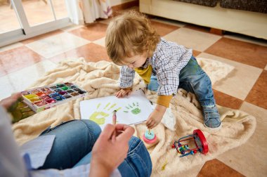 Bir anne ve çocuk, yaratıcı ifadeler ve ebeveyn sevinciyle dolu kapalı bir öğleden sonra, el boyaması sanat eserleri yaratmak için kaliteli zaman harcarlar..