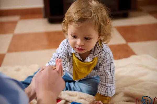 Dişli gömlek ve sarı önlük giymiş, yumuşak bir yüzeyde mutlu mesut oynayan bir çocuk. Parlak bir ortam hoş ve neşeli bir atmosfer sergiliyor..