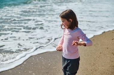 Okyanus dalgaları parlak güneşli bir günde kıyıya yaklaşırken genç bir kız sahilde duruyor, doğanın tadını çıkarıyor..
