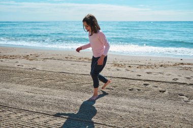 Neşeli bir çocuk kumsalda oynuyor, arka planda mavi okyanus dalgalarıyla güneşin tadını çıkarıyor..