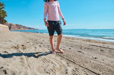 Sakin bir okyanusun kenarındaki kumlu sahilde çıplak ayakla yürüyen genç, güneşli bir günün ve doğanın tadını çıkarıyor..