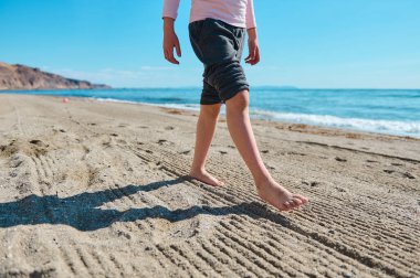 Deniz kenarındaki el değmemiş kumsalda çıplak ayaklı bir birey, dinginliği ve yaz neşesinin özünü resmediyor..