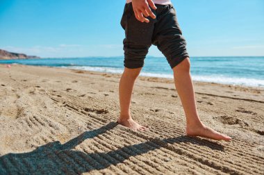 Kumlu sahilde çıplak ayakla yürüyen kişi, parlak, berrak, mavi gökyüzünün altında yaz güneşinin ve okyanus esintisinin tadını çıkarıyor..