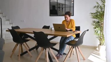 Kadın laptopuyla evden çalışıyor, modern dairesinin sessizliğinin ve huzurunun tadını çıkarıyor..