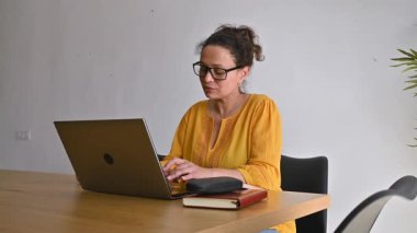 Modern ev ofisinden uzaktan çalışan bir kadın. Masasında dizüstü bilgisayarında yazıyor..