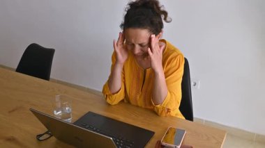 Stres ve anksiyete yaşayan bir kadın ilaç alır. O, dizüstü bilgisayarı, telefonu ve bir bardak su ile masasında oturuyor..