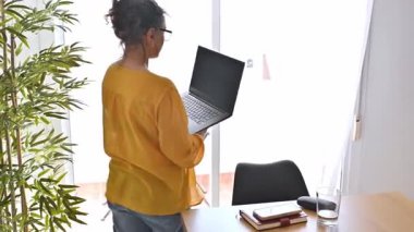 Evde dizüstü bilgisayarıyla çalışan bir kadın. Dizüstü bilgisayarı alır ve JPP 'yi ayakta çalışmak için yeni bir yere götürür..