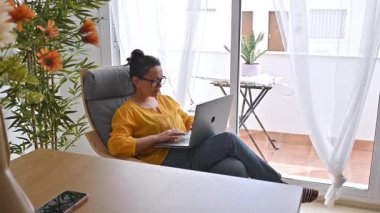 Evden çalışan bir kadın. Dizüstü bilgisayar kullanıyor ve oturma odasında verimli bir çalışma yapıyor..