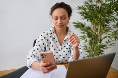 Uzaktan kumandalı, akıllı telefon ve dizüstü bilgisayar kullanan serbest girişimci. Modern dekore edilmiş bir yerde dijital göçebelerin yararlarını gösteren sanal çalışma ortamlarını destekleyen bir kadın..