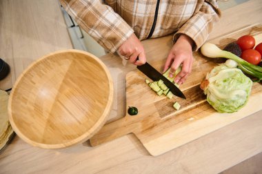 Tahta tezgahta taze sebzelerle sağlıklı bir salata hazırlamak, sağlıklı yemekleri ön plana çıkarmak. Salatalık, salatalık, domates ve ahşap bir kase ile kesim tahtası sahneyi güçlendirir..